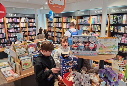 Die Kinder schauen sich die Bücher und andere Gegenstände in der Buchhandlung an, ein Junge guckt erstaunt in die Kamera