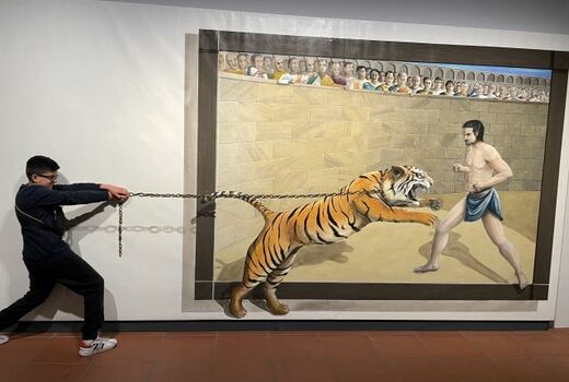 Illusion: Auf einem großen Bild will ein Tiger einen Gladiatoren anfallen. Ein Schüler steht rechts und hält den Tiger an einer Kette zurück.