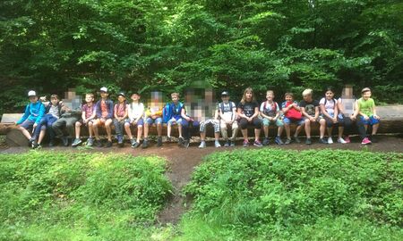 Gruppenfoto der Klasse 3 a und 3b alle sitzen auf einem langen Baumstamm in der Reihe.
