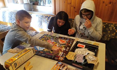 Eine Schülerin und zwei Schüler sitzen am Tisch und spielen Monopoly.