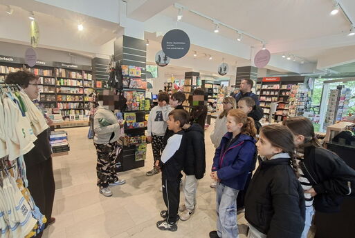 Die Kinder der Klasse werden in der Buchhandlung begrüßt und hören zu.