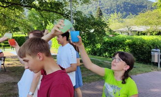 Jugendliche spielen ein Spiel mit Wasserbechern. Das Wasser wird über den Kopf in einen weiteren Becher gegossen.