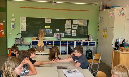 Fünf Schüler und eine Schülerin sitzen im Klassenzimmer an mehreren zu einem Gruppentisch zusammengeschobenen Tischen, auf denen Gegenstände zum Biber liegen