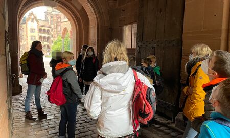 Eine Lehrerin erklärt einer Schulklasse etwas vor dem Eingang zum Innenhof des Heidelberger Schlosses