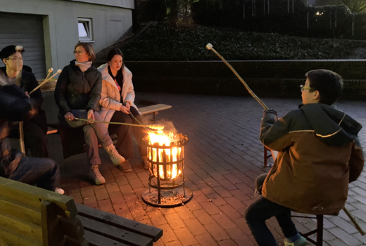 SchülerInnen und ErzieherInnen sitzen um einen Feuerkorb mit Stockbrot und Marshmallows