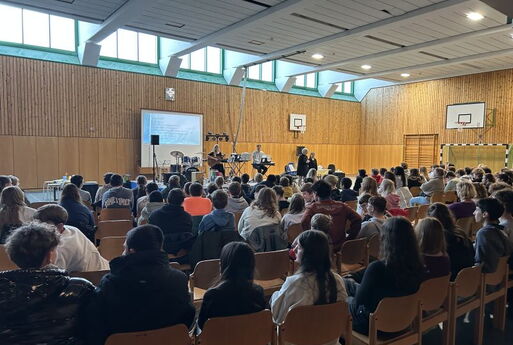 Viele SchülerInnen und Schüler singen in einer Turnhalle und schauen zur Bühne