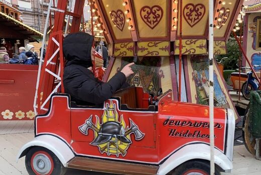 Ein Kind sitzt auf einem altmodischen Karussell in einem knallroten Feuerwehrauto.