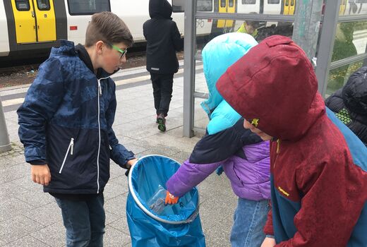 Schülerinnen sammeln Müll mit einer Greifzange auf und sammeln den Müll in einem blauen Sack