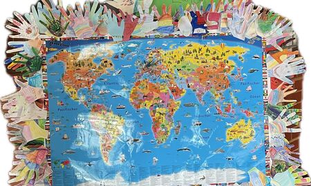 In der Mitte hängt eine Weltkarte. Außen herum sind viele bunt gestaltete Papierhände der Schülerinnen und Schüler angebracht. Oben hängt ein grünes Plakat mit dem Text: Eine Abteilung - viele Länder.