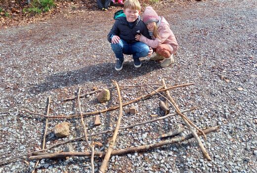 Zwei Kinder betrachten ein selbstgebautes Spiel aus Stöcken und Steinen