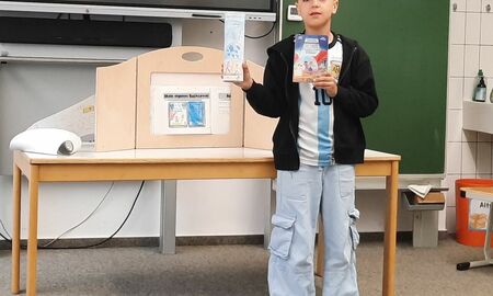 Ein Schüler steht vorne im Klassenzimmer und präsentiert seine Leserolle zum Buch "Mission Roboter".