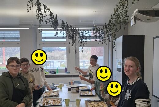 Sieben Schüler sitzen bzw. stehen an einem Tisch. Ebenso viele Bleche mit Plätzchen befinden sich auf dem Tisch.