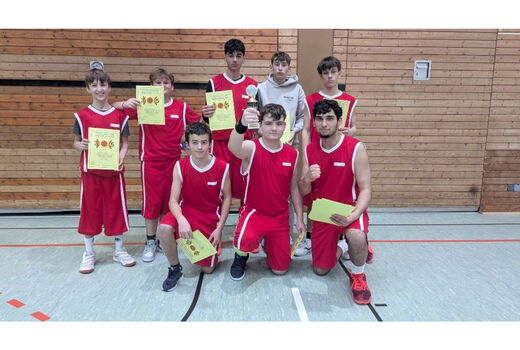 Gruppenfoto mit acht Basketballern. Sie halten ihre Urkunden hoch, einer die Trophäe. Drei Jungs knien im Vordergrund. Hinten stehen fünf weitere