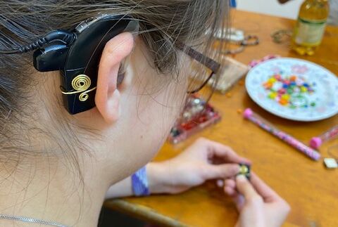 Eine Schülerin zeigt ihren gebastelten Schmuck der an ihrem Cochlear Implantat befestigt ist.