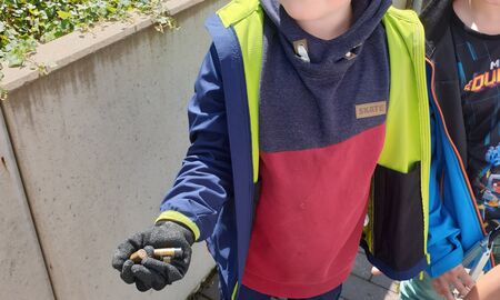 Ein Erstklässler mit Schutzhandschuh hält mehrere gefundene Batterien in der Hand.