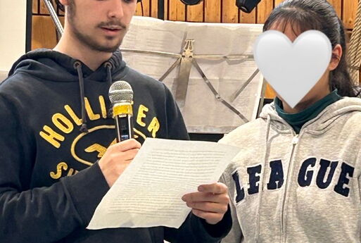 Ein Schüler und eine Schülerin lesen etwas auf einer Bühne vor