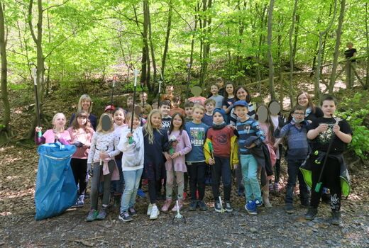 Gruppenfoto  im Wald von zwei dritten Klassen mit ihren Lehrerinnen und alle sind mit Handschuhen, Müllzangen und Mülltüten ausgestattet.