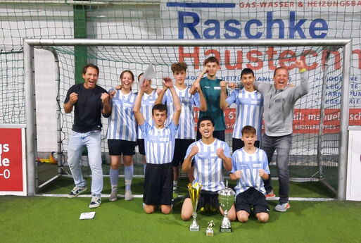 Die Schüler und Schülerinnen stehen mit ihren Trainern jubelnd in einem Fußballtor. Vor ihnen stehen drei Pokale.
