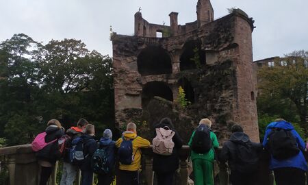 Neun Schülerinnen und Schüler schauen auf die Überreste eines zerstörten Turms des Heidelberger Schlosses.
