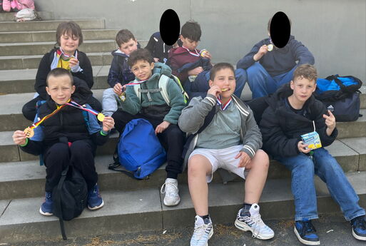 9 Jungs aus der Grundschule sitzen auf einer Treppe und halten Medaillen in die Kamera