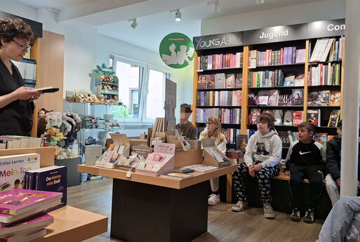 Die Buchhändlerin liest aus dem Buch vor und die Kinder hören zu