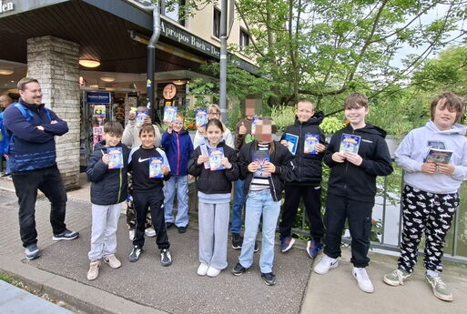 Die Klasse steht mit ihrem neuen Buch vor der Buchhandlung, sie lächeln und halten das Buch in die Kamera