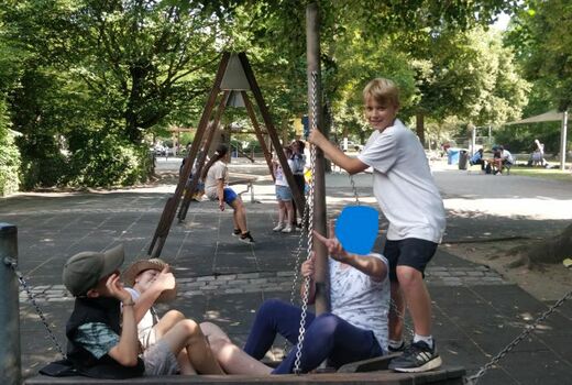 Vier Schüler haben Spaß auf einer Schaukel. Drei sitzen, einer steht und schaut lachend zur Kamera.