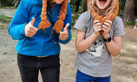 Eine Lehrerin und eine Schülerin posieren fröhlich mit Wikingerhüten mit orangenen Zöpfen. Sie haben zwei Beine zusammengebunden, sodass das linke Bein der Lehrerin und das rechte Bein der Schülerin nur zusammen bewegt werden können.