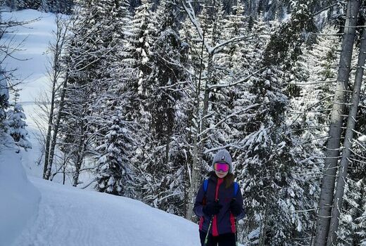 Ein Schneewanderer steht auf einem verschneiten Weg im Wald.