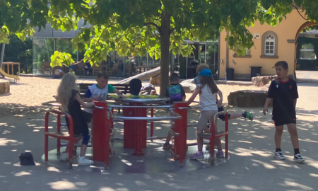 Auf dem Spielplatz im Heidelberger Zoo stehen mehrere Schüler und Schülerinnen auf einem sich drehenden Karusell. Ein weiterer Schüler läuft gerade daran vorbei.