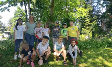 Lehrerin posiert mit 4 Schülerinnen und 6 Schülern für ein Gruppenfoto auf einer Wiese unter einem Baum