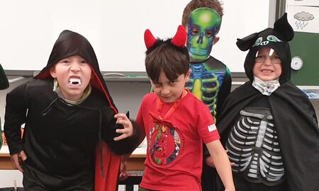 Vier Kinder posieren als Vampir, Teufel und Skelette verkleidet vor einer Tafel.