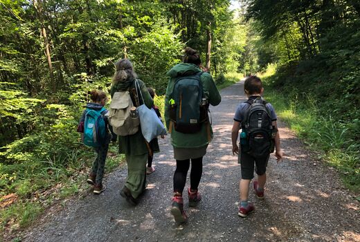 Zwei Kinder und zwei Frauen von hinten, die einen Waldweg entlang gehen