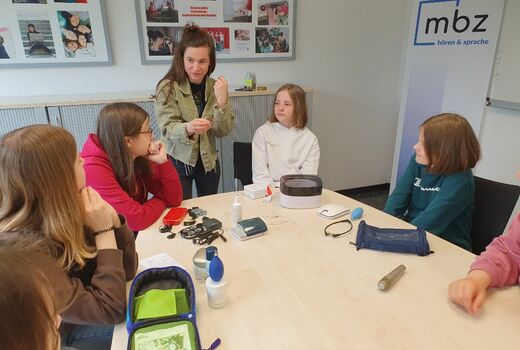 Eine Lehrerin erklärt einer Gruppe Mädchen etwas über Hörhilfen