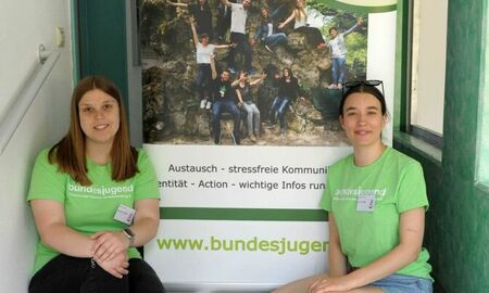 zwei junge Frauen der Bundesjugend sitzen vor ihrem Plakat