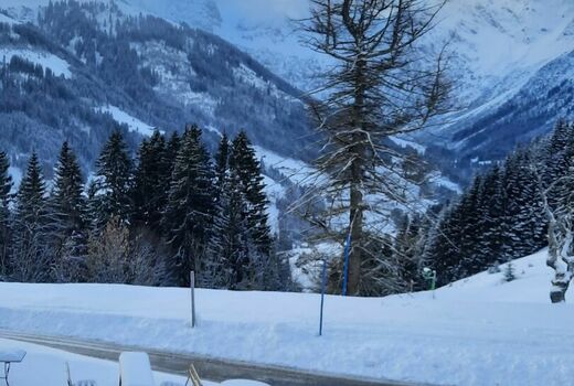 Im Vordergrund sieht man eine schneebedeckte Sitzgarnitur, im Hintergrund die verschneiten Berge.