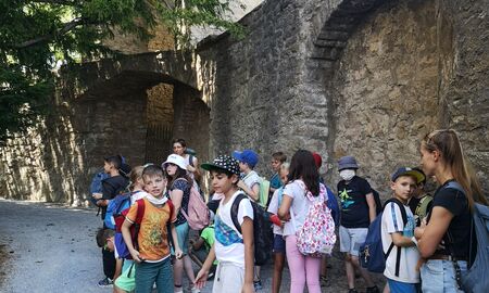 Zwei Lehrerinnen und viele Kinder stehen innerhalb der Burg bei einer hohen Burgmauer und einem großen Baum