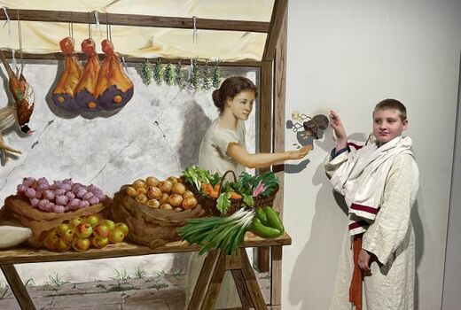 Illusion: Bild von einem Marktstand mit Fleisch, Gemüse und Obst. Ein Schüler lässt der römischen Marktfrau Münzen aus einem Beutel in die Hand fallen.