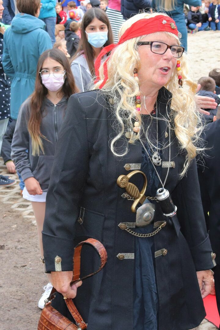 Eine Frau mit blonden Haaren und Kopftuch. Im Hintergrund zwei Mädchen.