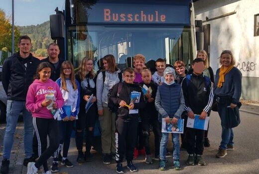 Elf Kinder und vier Erwachsene stehen vor einem Bus. Alle lachen in die Kamera.