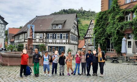 Die Klassenlehrerin und zehn Schüler und Schülerinnen posieren nebeneinander vor einem Brunnen auf einem Marktplatz umringt von Fachwerkhäusern.