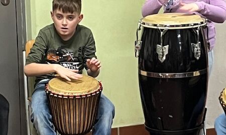 Ein Schüler und eine Schülerin sitzen oder stehen an unterschiedlichen Trommeln und trommeln einen Rhythmus.