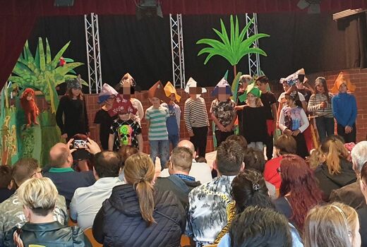 Die Schülerinnen und Schüler der dritten Klassen führen auf einer Bühne mit Palmen als Bühnenbild den neuen Erstklässlern, Erstklässlerinnen und deren Eltern mit gebastelten Piratenhüten ein Willkommensstück vor.