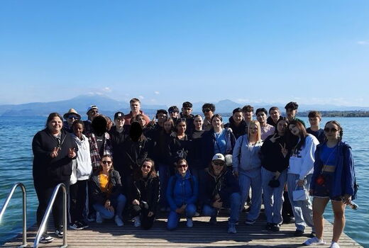 Gruppenbild mit Schülern und Lehrern. Sie stehen alle am Ende eines breiten Holzsteges. Im Hintergrund sieht man den See und schemenhaft Berge.