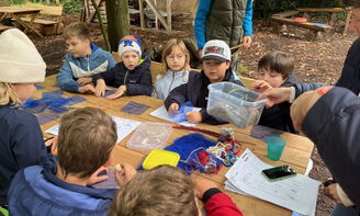 Kinder, in winterlicher Kleidung, sitzen im Freien an einem Holztisch.