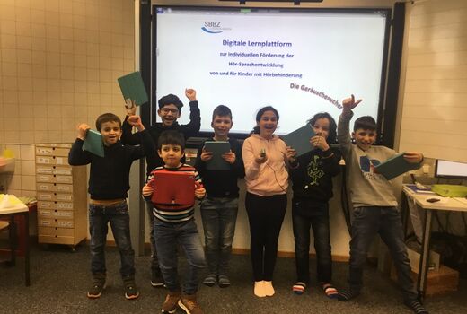 Sieben Schüler und Schülerinnen stehen vor der Leinwand auf der das Projekt zur digitalen Lernplattform gezeigt wird. Das Motto lautet die Gräuschesucher.