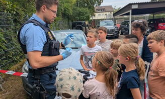 Der Polizist zeigt den Kindern wie man Spuren nimmt