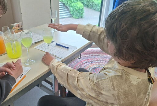Ein Kind legt seine Finger auf ein halb gefülltes Glas auf einem Tisch, daneben steht ein weiteres halb gefülltes Glas