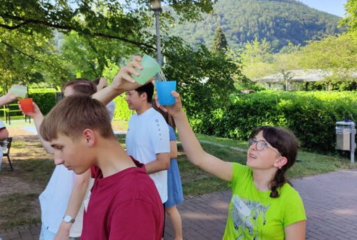 Jugendliche spielen ein Spiel mit Wasserbechern. Das Wasser wird über den Kopf in einen weiteren Becher gegossen.