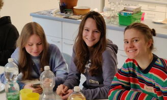 Drei Mädchensitzen am Tisch und lächeln